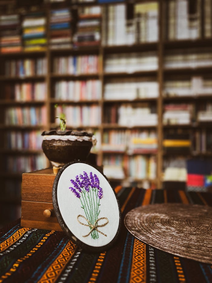 A cozy library interior featuring lavender embroidery art, bookshelves, and eclectic decor.